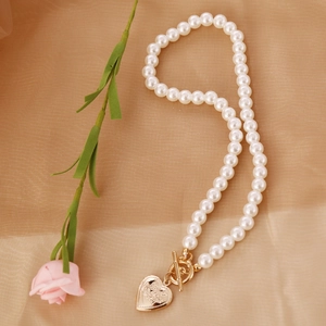 Elegant pearl necklace with golden heart pendant engraved I Love You on beige fabric