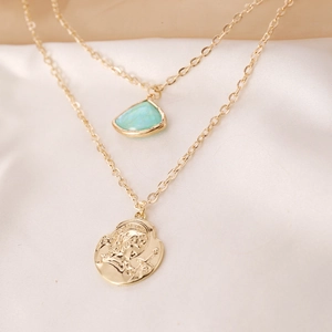 Detail of gold layered necklace with turquoise stone and embossed coin pendant on silk