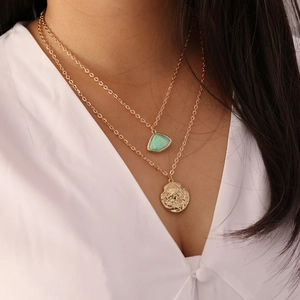 Layered gold necklace featuring a green semi-precious stone and a vintage coin pendant
