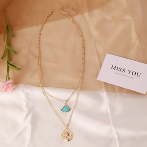 Detailed view of layered gold necklace with teal fan pendant and embossed coin charm