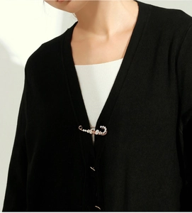 Close-up of rose gold safety pin brooch with white crystals on black cardigan sweater