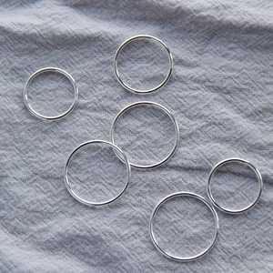 Set of six minimalist polished silver stacking rings on soft textured fabric background