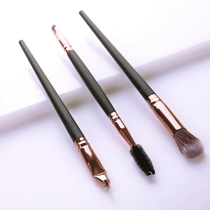 Detail of three professional makeup brushes with black matte handles and rose gold ferrules