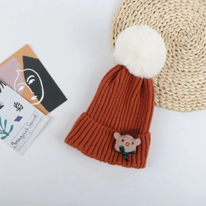 Détail du bonnet en maille avec pompon en fausse fourrure blanche et patch renne
