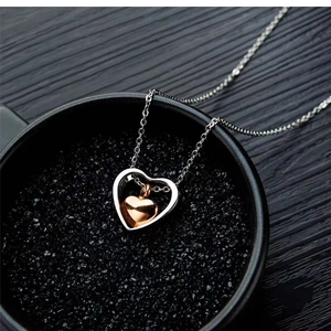 Detail of silver hollow heart pendant with rose gold inner heart on black texture