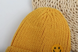 Dettaglio di un berretto in maglia giallo brillante con toppa ricamata a smile
