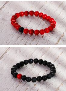 Close-up of 8mm matte black agate and red stone beaded bracelets on white wood background