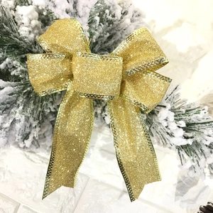 Close-up of a glittering gold Christmas bow ornament on snow-covered pine branches