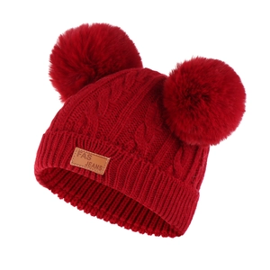 Close-up of red cable knit kids beanie with double faux fur pom-poms and leather patch