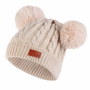 Detail of chunky knit baby hat with two pink pom-poms and leather logo patch in beige