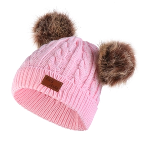Detail of pink cable knit baby hat featuring double faux fur pom-poms and leather logo patch