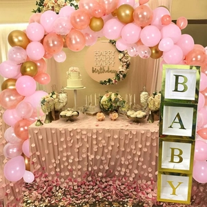 Detail of four transparent baby shower gift boxes with gold trim and pink balloon arch
