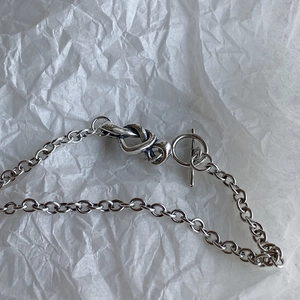 Close-up of silver chain bracelet featuring a unique knot design and T-bar toggle clasp