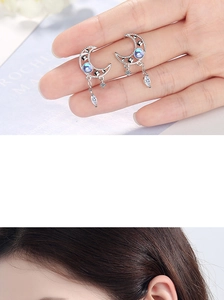 Detail of silver crescent moon earrings with blue crystal star and tassel drop charms