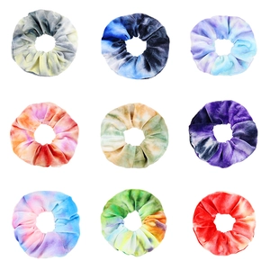 Flat lay of nine tie-dye velvet hair scrunchies in vibrant gradient colors on white background