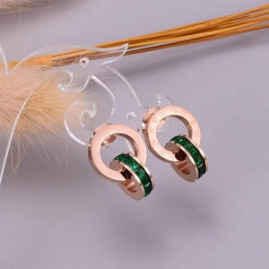Close-up of rose gold double ring earrings with Roman numerals and emerald green stones