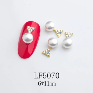 Macro detail of alloy nail charm with white faux pearl and AB crystal in gold base