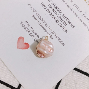 Detailed view of baroque irregular pinkish pearl pendant with gold plated edge on a card
