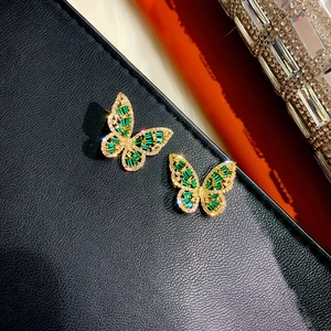 Detailed close-up of butterfly zircon earrings with green gems on black leather
