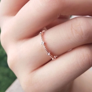 Minimalist rose gold ring featuring four tiny diamonds worn on a finger in soft light
