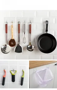 Detail of transparent adhesive hooks holding various kitchen tools on white tile walls