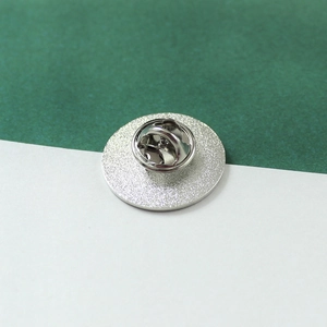 Silver metal planet badge shown from the back featuring a secure butterfly clutch fastener