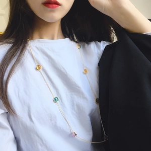 Long golden necklace with colorful crystal square charms worn by model over a black blazer