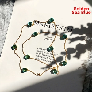 Detailed view of long gold chain necklace with emerald cut sea-blue crystals on a white page
