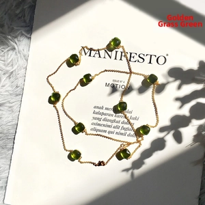 Detailed macro shot of a long golden necklace featuring faceted grass green crystal stones