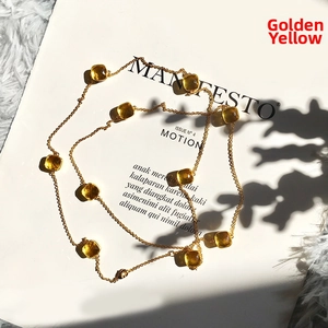 Detail of long golden necklace featuring square-cut yellow crystal gemstones on a white prop