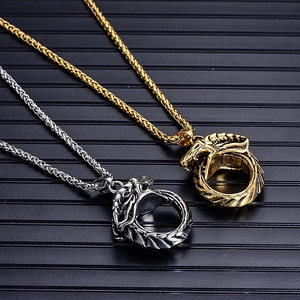 Detail of Ouroboros dragon ring pendants in gold and silver finish on textured black surface