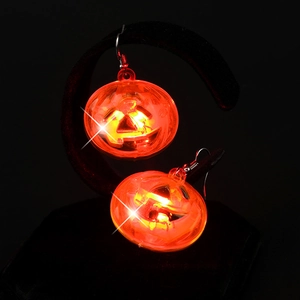 Close-up of glowing LED pumpkin earrings for Halloween on a professional black display