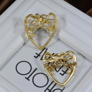 Detailed close-up of matte gold vintage heart brooch with cupid relief and pearls