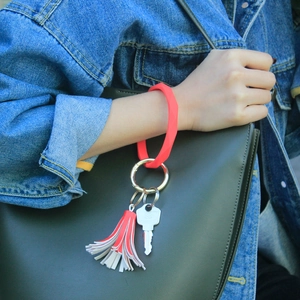 Detail of red silicone wristlet keychain with tassel on wrist with denim jacket