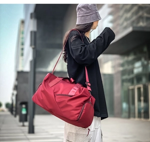 Red waterproof travel bag worn by a model on a city street during outdoor activities