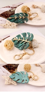 Macro details of green monstera leaf keychain with gold veins on white sand background