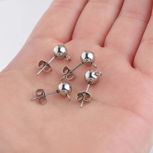 Five silver stainless steel ball stud earrings with loops held in hand for jewelry DIY