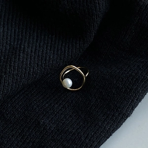 Close-up of minimalist gold twisted wire ring with a round white pearl on black fabric