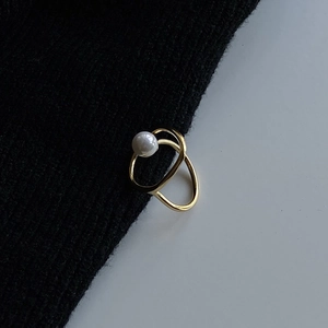 Detailed view of an irregular gold double-ring with a white pearl on black fabric