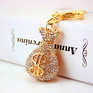 Golden money bag keychain with sparkling rhinestones and dollar sign on a white book