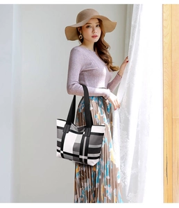 Detail of a large black and white plaid tote bag with black handles carried by a model
