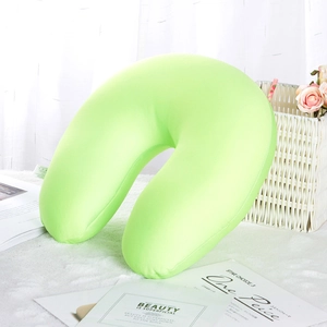 U-shaped light green travel neck pillow on a soft white plush background with decor