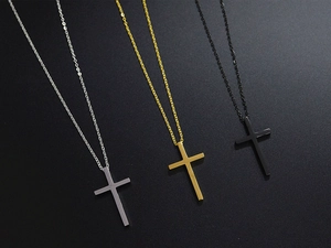 Detailansicht der Kreuzanhänger in Silber, Gold und Schwarz auf dunkler Sandstruktur