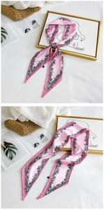 Detailed view of pink floral long silk scarf styled on white linen with a straw bag