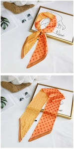 Detailed view of an orange gradient polka dot silk scarf tied as a bow on a bag