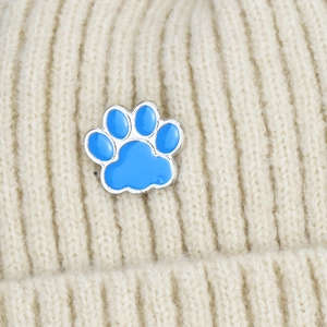 Blue enamel cat paw pin badge styled on a beige knitted beanie hat detail view