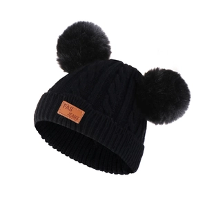 Close-up of winter knit hat with fluffy black faux fur pom-poms and brown leather patch