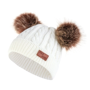 Detailed knit texture of children winter hat with dual faux fur pom-poms and leather tag