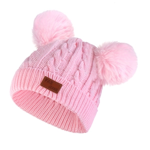 Detail of pink knitted winter hat featuring dual fluffy pompoms and a leather patch
