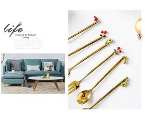 Detail of golden stainless steel spoons with decorative enamel fruit charms on handles